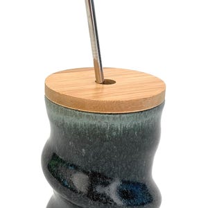 May include: A dark green ceramic mug with a wood lid and a metal straw. The mug has a unique swirl design.