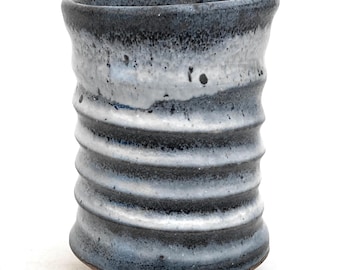 May include: A black and white ceramic cup with a textured, ribbed design. The cup has a wide mouth and a rounded base.