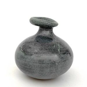 May include: A small, round, gray ceramic vase with a unique, slightly tilted opening.