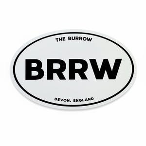 May include: White oval sticker with black text. The text reads "THE BURROW" at the top, with "BRRW" in large bold letters in the centre, and "DEVON, ENGLAND" at the bottom. The sticker has a black border.