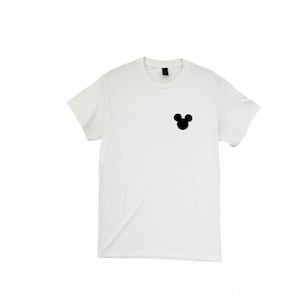 Puede incluir: Una camiseta blanca con una silueta negra de la cabeza de Mickey Mouse en la parte superior izquierda del pecho. La camiseta tiene mangas cortas y cuello redondo. La camisa es de un material suave y opaco.