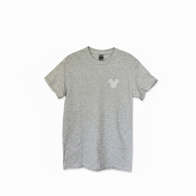 Puede incluir: Una camiseta gris jaspeado con un peque&ntilde;o gr&aacute;fico de la cabeza de Mickey Mouse en gris claro en el lado izquierdo del pecho. La camiseta de manga corta tiene cuello redondo y est&aacute; hecha de un material suave y c&oacute;modo. Un estilo cl&aacute;sico y casual.