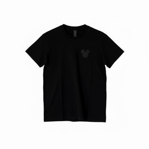 Puede incluir: Camiseta negra lisa con un peque&ntilde;o gr&aacute;fico tonal de la cabeza de Mickey Mouse en el pecho izquierdo. La camiseta tiene cuello redondo cl&aacute;sico y mangas cortas. La tela parece ser suave y c&oacute;moda.