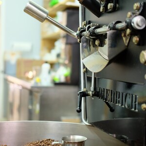 May include: A close-up of a coffee roaster with a silver cup of roasted coffee beans inside. The roaster is black with the word "DIEDRICH" printed on the side.