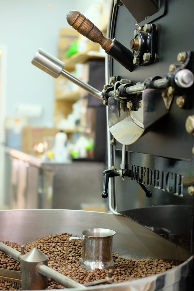 May include: A close-up of a coffee roaster with a silver cup of roasted coffee beans inside. The roaster is black with the word "DIEDRICH" printed on the side.
