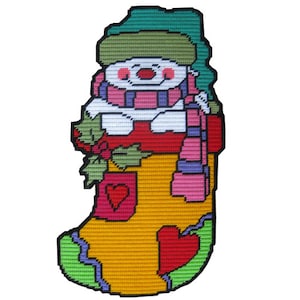 May include: A yellow Christmas stocking with a snowman inside. The snowman is wearing a green hat, a pink scarf, and a white body. The stocking has a red heart and green holly.