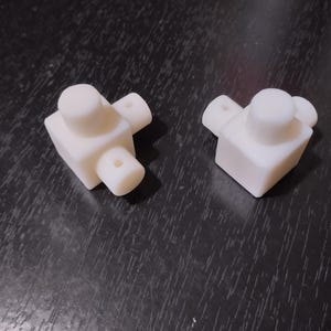 Può includere: Due pezzi di raccordo angolare bianchi tridimensionali, ciascuno caratterizzato da una base cubica centrale con tre sporgenze cilindriche che si estendono da facce diverse, con ogni sporgenza che presenta un piccolo foro circolare all'estremità.