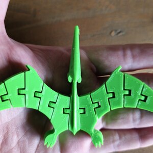 May include: A green 3D printed model of a pterodactyl with articulated wings. The model is made of plastic and has a detailed design.