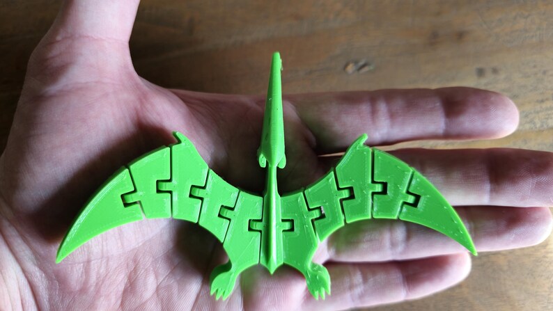 May include: A green 3D printed model of a pterodactyl with articulated wings. The model is made of plastic and has a detailed design.