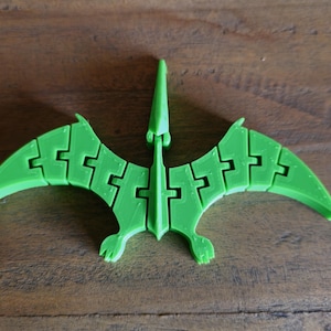 May include: A green plastic pterodactyl puzzle toy. The toy is made up of interlocking pieces that form the shape of a pterodactyl.