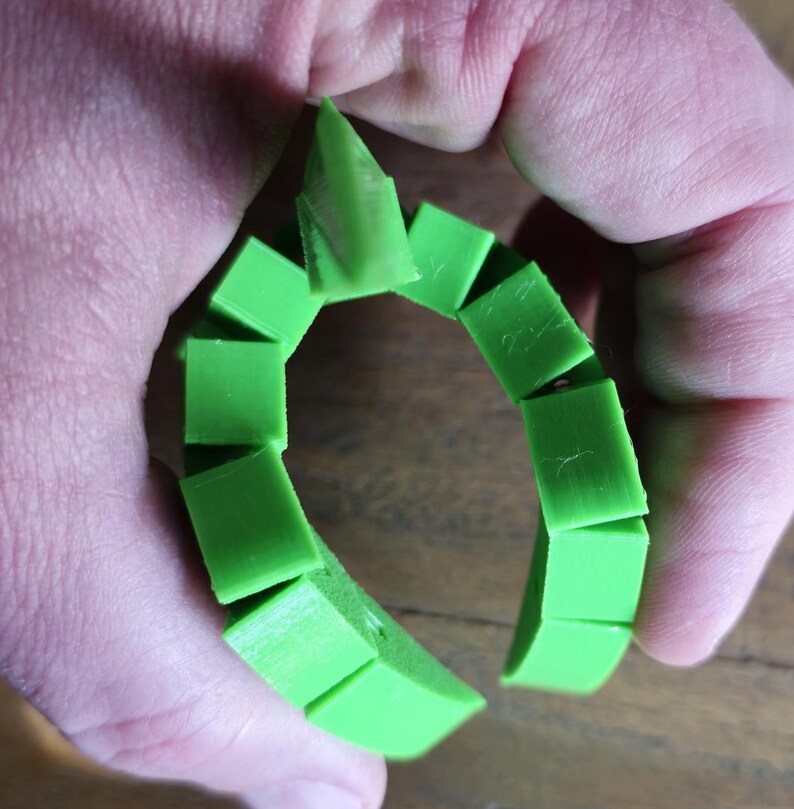 May include: A green plastic ring made of interlocking pieces. The ring is open and can be adjusted to fit different sizes.