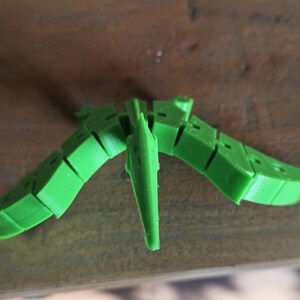May include: A green 3D printed model of a pterodactyl, a flying reptile with a long beak and wings.