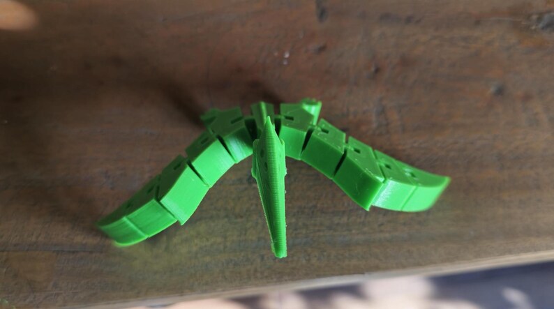 May include: A green 3D printed model of a pterodactyl, a flying reptile with a long beak and wings.