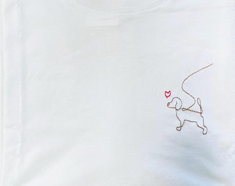 May include: A white t-shirt with a brown embroidered dog design. The dog is holding a red heart in its mouth.