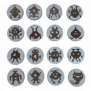 Op de afbeelding: Zestien ronde houten ornamenten met gepixelde alien-ontwerpen. Elk ornament heeft een klein gaatje om op te hangen. De aliens zijn donkerbruin, tegen een lichtgrijze achtergrond. Ideaal voor knutselen of als decoratie.