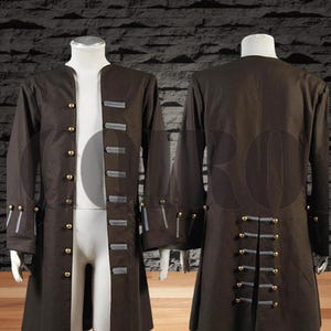 Può includere: Un lungo cappotto marrone con bottoni dorati e dettagli grigi, esposto su un manichino. Il cappotto ha maniche lunghe e una vestibilità su misura, con dettagli di bottoni decorativi sui polsini e sulla schiena.
