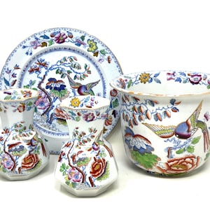 May include: A collection of white porcelain items with a floral and bird design. The set includes a large bowl, a plate, and several vases. The color palette features red, blue, yellow, and green accents, creating a vibrant and detailed aesthetic.