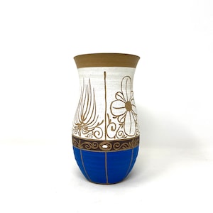 May include: A white ceramic vase with brown and blue accents. The vase has a floral design and a textured surface.