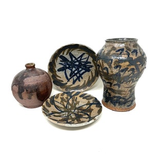 May include: A set of four ceramic pottery pieces in brown, black, and white with abstract designs. The set includes a small vase, a larger vase, and two plates.