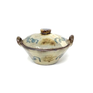 May include: A small, white ceramic pot with a lid and two handles. The pot has a brown glaze and blue floral designs.