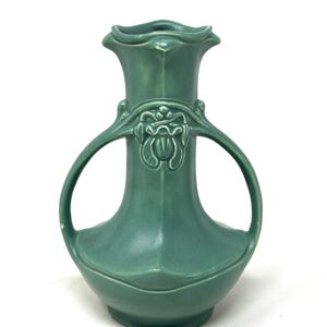 May include: A green ceramic vase with two handles and a floral design. The vase has a wide base and a narrow neck.