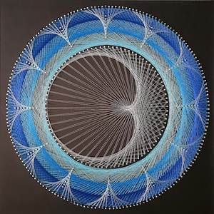 May include: A circular string art piece with a white background and blue and light blue string. The string is arranged in a pattern of concentric circles and radiating lines.