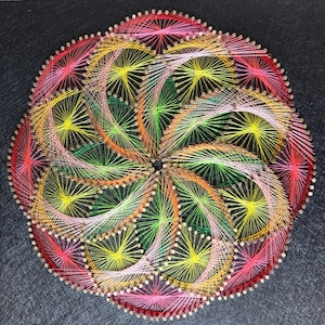 May include: A colorful string art design with a circular pattern of red, pink, yellow, green, and orange thread wrapped around nails on a black background.