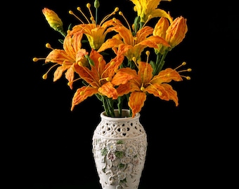 May include: A bouquet of vibrant orange lilies with dark speckles and long yellow-tipped stamens arranged in a cream-colored ceramic vase featuring intricate cut-out patterns and embossed floral details on its exterior surface.