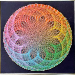 May include: A colorful string art piece in a circular shape with a rainbow color scheme. The art is framed in a black frame with a gold trim.