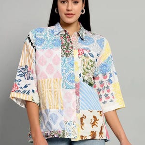 Op de afbeelding: Een overhemd met knoopsluiting en een patchwork-ontwerp met diverse kleurrijke patronen, waaronder bloemmotieven, strepen en tijgerillustraties. Het overhemd heeft een klassieke kraag, driekwartmouwen en een witte basis met accenten in blauw, roze, geel en groen.