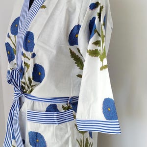 May include: White cotton robe with blue floral print and blue and white striped trim. The robe has a tie belt and a pocket.