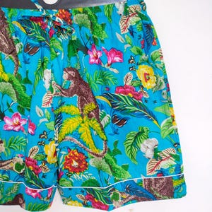 May include: Turquoise shorts with a jungle-themed print, including monkeys, flowers, and foliage. The shorts have a drawstring waist and white trim. The fabric is a bright turquoise colour.