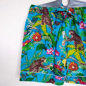 May include: Turquoise pajama shorts with a jungle-themed print of monkeys, flowers, and leaves. The shorts have a white trim and an elasticated waistband. The fabric is a bright blue colour.