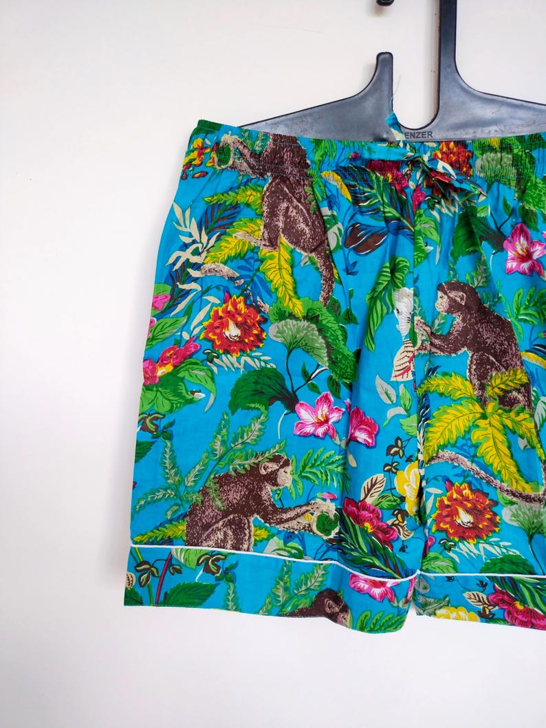 May include: Turquoise pajama shorts with a jungle-themed print of monkeys, flowers, and leaves. The shorts have a white trim and an elasticated waistband. The fabric is a bright blue colour.