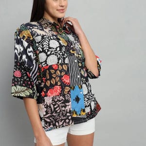 Op de afbeelding: Een overhemd met knoopsluiting en een patchwork-ontwerp met diverse bloemmotieven, botanische en geometrische patronen in zwart, wit, rood, geel en blauw. Het overhemd heeft een klassieke kraag, driekwartmouwen en een losse, ontspannen pasvorm.
