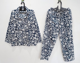 May include: A two-piece pajama set featuring a long-sleeved button-down shirt with a collar and a chest pocket, paired with matching elastic-waist trousers. Both pieces are navy blue with a repeating white floral and vine pattern throughout.