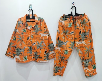 May include: A long-sleeved button-down shirt and matching elastic-waist pants set in bright orange. The fabric features a repeating jungle print with green palm trees, white and black zebras, spotted cheetahs, and toucans with black and yellow beaks.