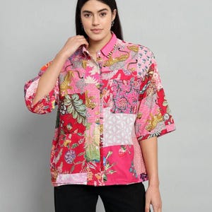 May include: A button-down shirt featuring a vibrant patchwork design in shades of pink and red. The pattern includes various floral motifs, geometric shapes, and illustrations of leopards. The shirt has a collar, a front pocket, and elbow-length sleeves.