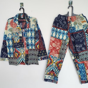 Peut inclure: Un ensemble de pyjama deux pièces avec un motif patchwork. Le haut est une chemise boutonnée avec un col et une poche poitrine. Le pantalon est droit. Le motif comprend des motifs géométriques et floraux bleus, rouges et jaunes sur fond crème.