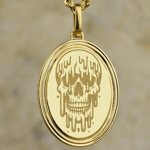 May include: Gold-colored pendant necklace featuring a detailed skull design. The skull has a melting effect, with the top of the skull appearing to drip. The pendant is round and has a rope chain. The jewelry is likely made of gold.
