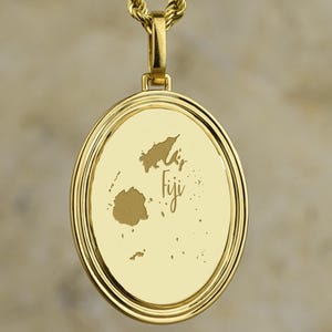 May include: A gold-colored pendant necklace featuring a detailed map of Fiji. The pendant is round with a textured border and hangs from a matching rope chain. The word "Fiji" is inscribed on the pendant.