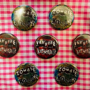May include: Six round buttons with a black and white collage design. The buttons feature the words "Zombie Kissed" and "Vampire Kissed".