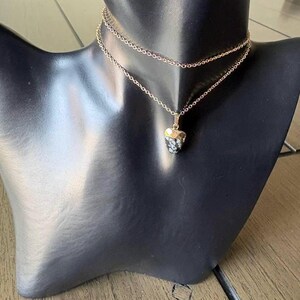 May include: A double-layered gold-tone chain necklace featuring a small, triangular-shaped pendant made of black and white snowflake obsidian stone. The necklace is displayed on a black mannequin bust, showcasing the delicate metal links.