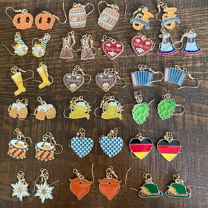 May include: A selection of Oktoberfest-themed earrings. The earrings showcase diverse designs, such as pretzels, beer steins, barrels, accordions, hearts, and traditional German attire. The earrings are made of metal and have gold-coloured hooks.