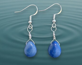 May include: A pair of drop earrings featuring smooth, teardrop-shaped blue stones suspended from silver-toned metal hooks. Each stone is secured with a delicate wire-wrapped setting that connects to a small silver bead and a simple ear wire.