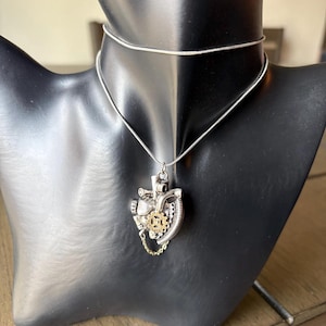May include: A silver-toned steampunk heart pendant necklace. The pendant features a detailed mechanical heart design with gears, chains, and intricate metalwork. The necklace is displayed on a black mannequin.