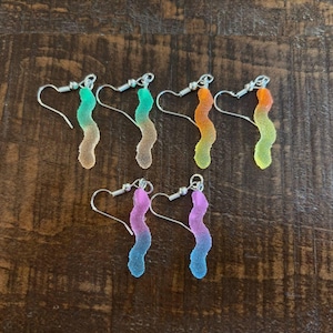 Könnte beinhalten: Sechs Paar neuartige Ohrringe in Form von bunten Gummibärchen. Jeder Ohrring hat einen Farbverlauf, darunter Grün, Orange, Gelb, Rosa und Blau. Die Ohrringe haben silberfarbene Fischhaken-Ohrdrähte.