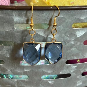 Op de afbeelding: Een paar gouden oorhangers met blauwe gefacetteerde edelsteen druppels. De oorbellen hebben een eenvoudig ontwerp en zijn perfect voor dagelijks gebruik.