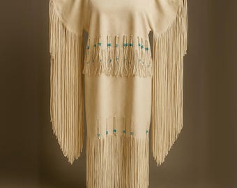 May include: Cream-colored suede dress with long fringe sleeves and hem. The dress features turquoise bead accents and a round neckline with a braided trim. The dress is displayed on a mannequin.