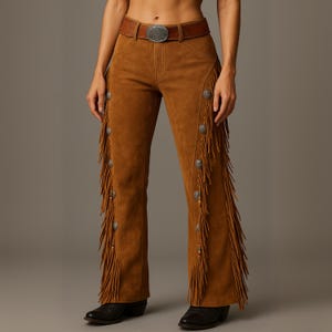 May include: Brown suede trousers with decorative fringe along the sides and silver-toned buttons. The trousers have a brown leather belt with a silver buckle. The trousers are worn with black boots.